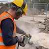 Groundworker wearing 24dB folding ear defenders and PPE gloves while using a concrete breaker on site