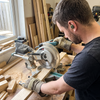 Carpenter wearing M20 electronic in-ear hearing protection earbuds and PPE gloves while using a mitre saw