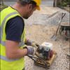 Groundworker wearing M20 electronic in-ear hearing protection earbuds and PPE gloves while using a plate compactor