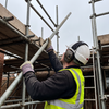 Scaffolder wearing NRR22 electronic Bluetooth ear muffs and PPE gloves while lifting a scaffold tube